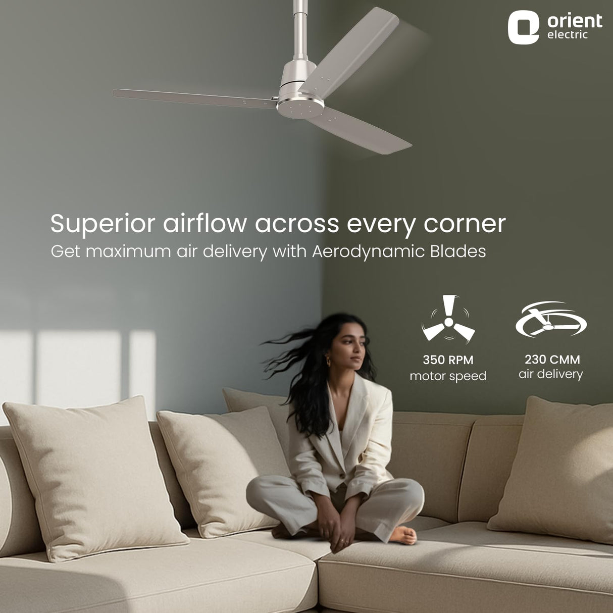 Woman sitting on a couch with a ceiling fan above, featuring Orient Electric branding.