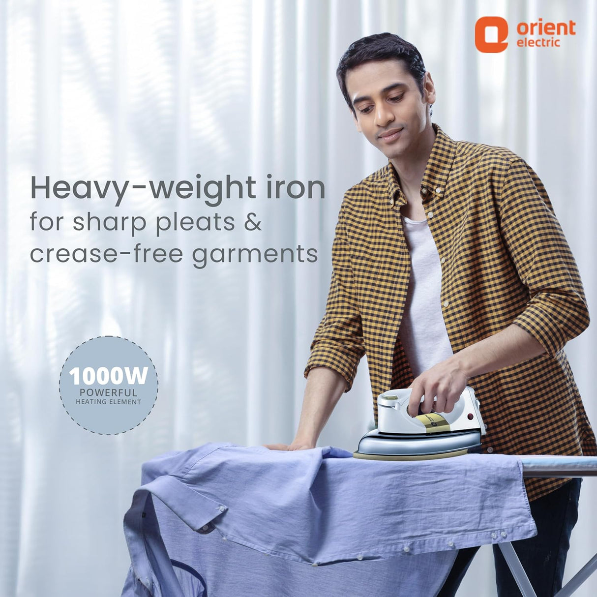 Person ironing clothes with an Orient Electric iron, against a white curtain background.