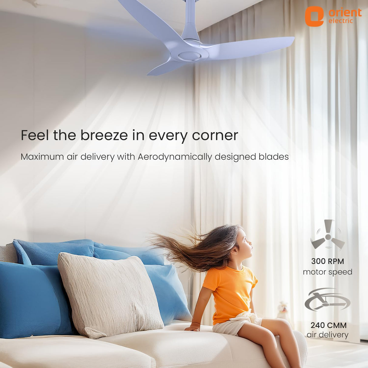 Ceiling fan in a room with a child sitting on a couch, featuring Orient Electric branding.