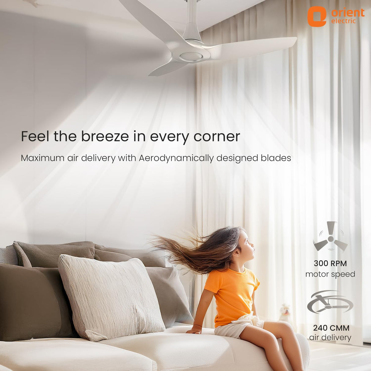 Living room with a ceiling fan and child enjoying the breeze, Orient Electric branding visible.