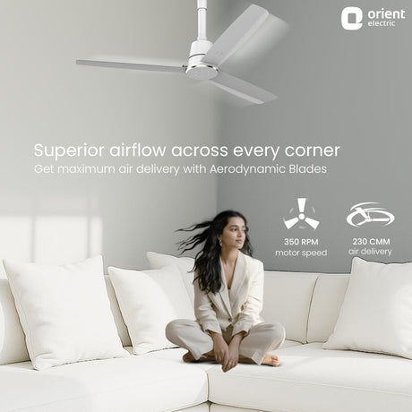 Woman sitting on a white couch with an orient electric ceiling fan above, featuring text about superior airflow.