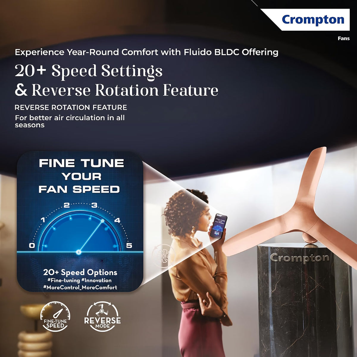 Crompton BLDC fan in a modern room setting, shown with a woman holding a phone to adjust its speed via a companion app. The fan has a distinctive curved, sculptural design in a warm metallic bronze color.