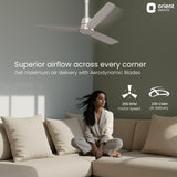 Woman sitting on a couch with a ceiling fan above, featuring Orient Electric branding.