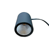 A black cylindrical LED light or lamp with a textured clear lens, resting on a wooden desk with a power cord extending to the right.