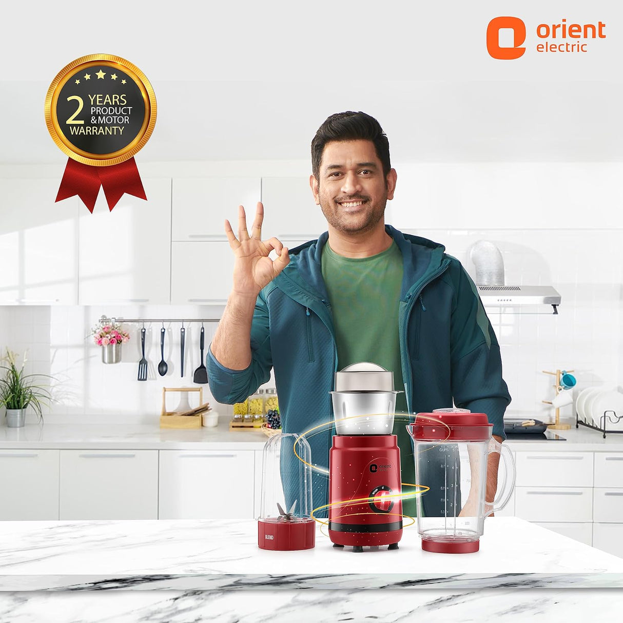 Man in a kitchen with a red Orient Electric blender, showing an 'ok' sign.