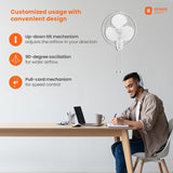 Person sitting at a desk with a laptop, wearing headphones, and a wall-mounted fan above them. Orient Electric branding is visible.