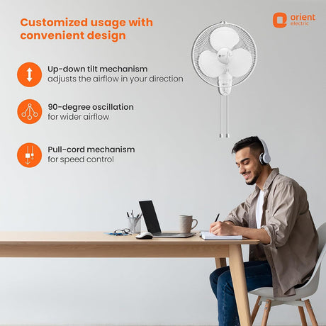 Person sitting at a desk with a laptop, wearing headphones, and a wall-mounted fan above them. Orient Electric branding is visible.