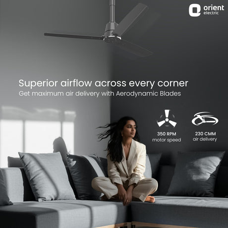 Woman sitting on a couch with a ceiling fan above, featuring Orient Electric branding.