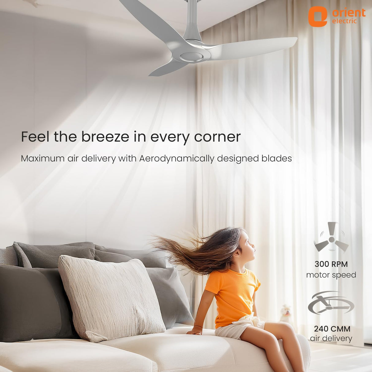 Ceiling fan in a room with a child sitting on a couch, featuring Orient Electric branding.