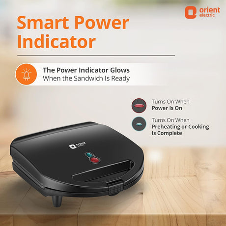 Black sandwich maker with Orient Electric logo on a wooden surface, featuring a smart power indicator.