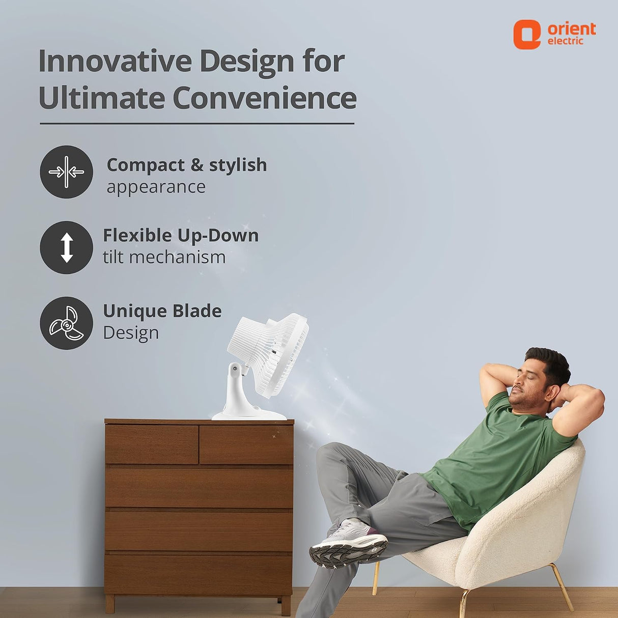 Man relaxing in a chair next to a white fan with Orient Electric branding.