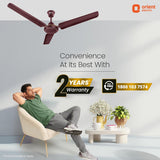 Man relaxing in a chair with a ceiling fan above, featuring Orient Electric branding.