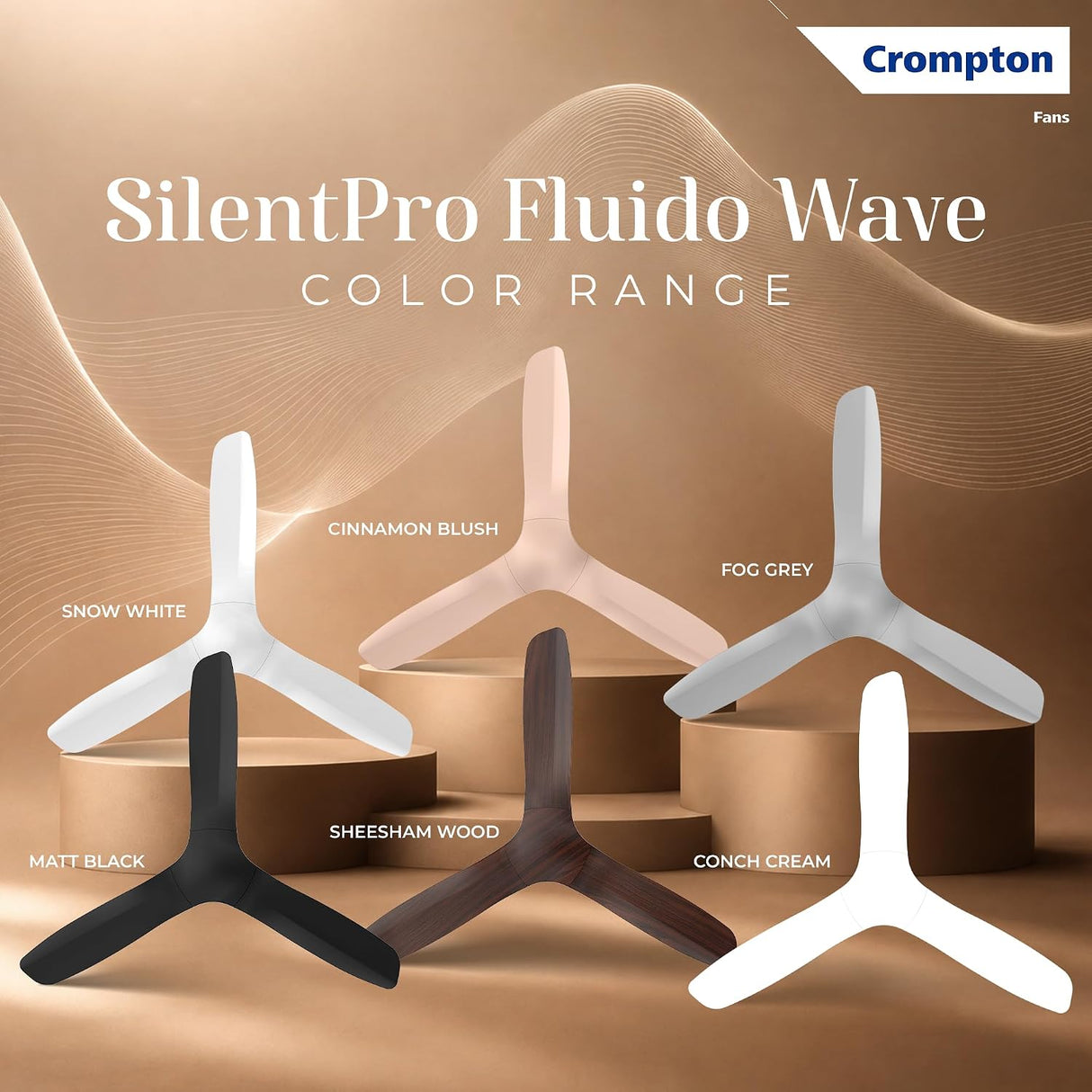 Crompton SilentPro Fluido Wave color range display featuring five Y-shaped desk fans in different finishes: Snow White, Cinnamon Blush, Fog Grey, Matt Black, Sheesham Wood, and Conch Cream, arranged on brown display pedestals against a warm beige background.