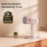 Pink handheld vacuum cleaner shown on a countertop with dimension labels (180mm width, 80mm depth, 200mm height) and a 2-year warranty badge. The background is a warm beige wall with soft shadows.