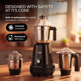 A black and stainless steel electric blender set displayed on a wooden table in a warm kitchen setting, with three jars and marketing text on the left.
