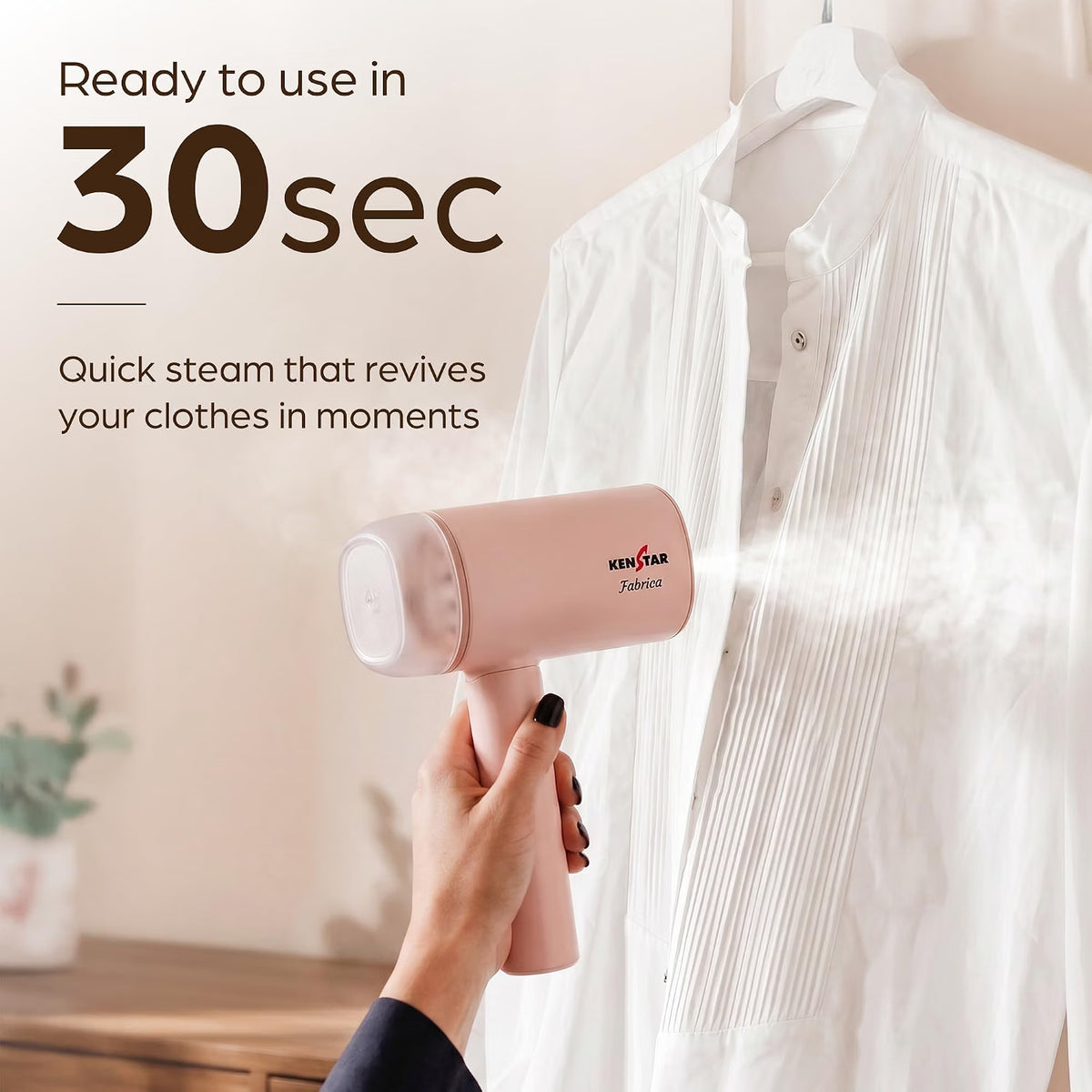 A pink handheld garment steamer is being used by a hand to steam a white pleated button-up shirt. The image includes marketing text that reads 'Ready to use in 30sec Quick steam that revives your clothes in moments' and shows the brand name 'KENSTAR' on the steamer.
